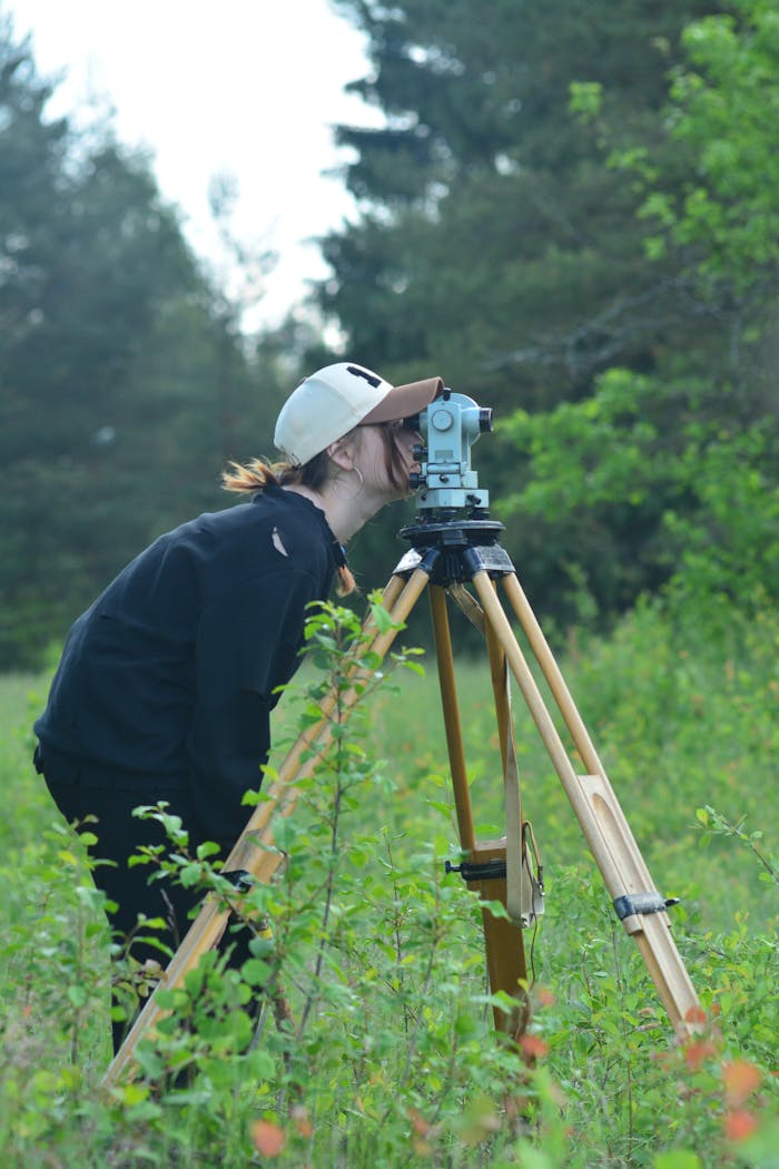 who-we-are Surveyor using theodolite for measurements in outdoor forested area.
